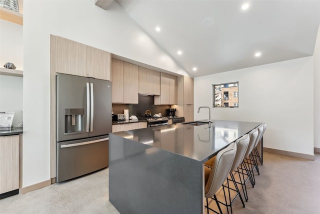 kitchen featuring light brown cabinets, a sink, stainless steel appliances, dark countertops, and a kitchen breakfast bar