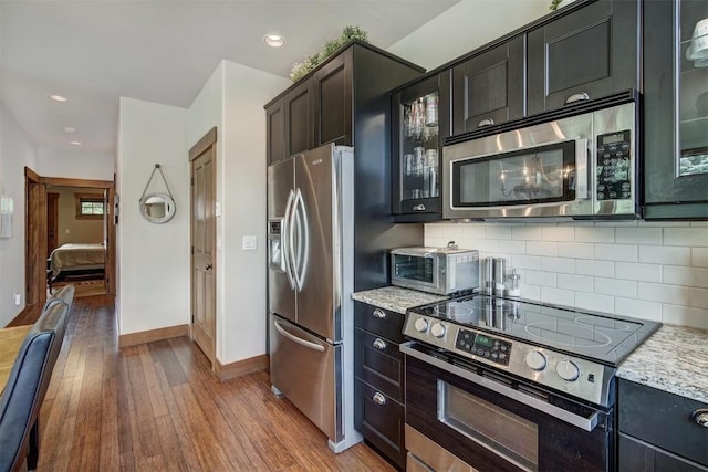 kitchen featuring tasteful backsplash, light stone counters, wood-type flooring, and appliances with stainless steel finishes