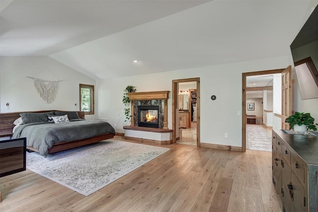 bedroom with light wood-type flooring, a fireplace, baseboards, and lofted ceiling