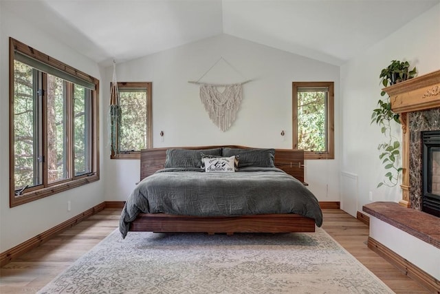 bedroom with vaulted ceiling, light wood-type flooring, a fireplace, and baseboards