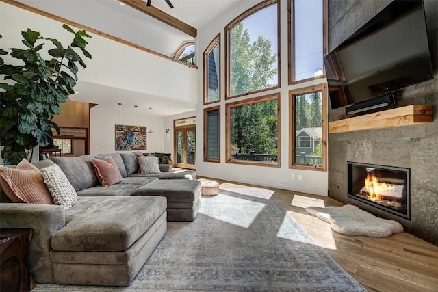 living room featuring a towering ceiling, beam ceiling, wood finished floors, and a glass covered fireplace