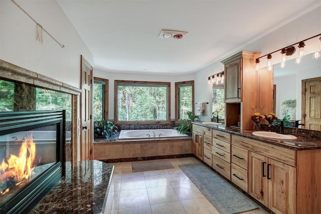 full bath with double vanity, tile patterned floors, a garden tub, a fireplace, and a sink