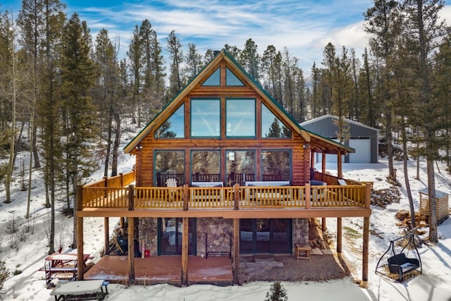 snow covered house with a deck, stone siding, and an outdoor structure