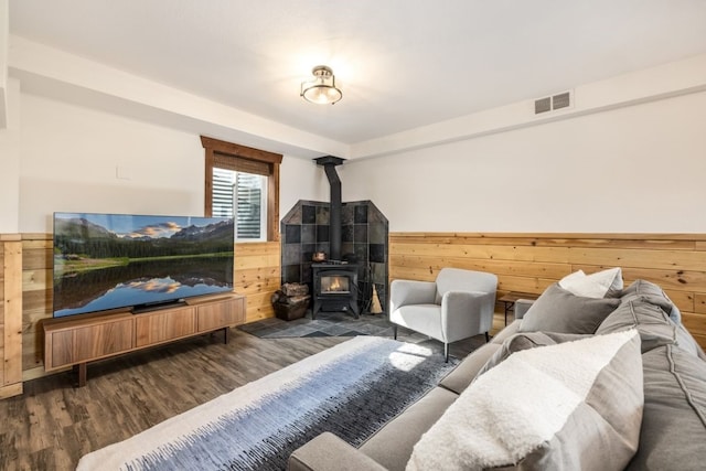 living area with visible vents, wainscoting, wood finished floors, a wood stove, and wood walls