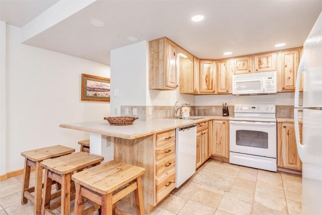 kitchen featuring a breakfast bar, light brown cabinets, white appliances, sink, and kitchen peninsula