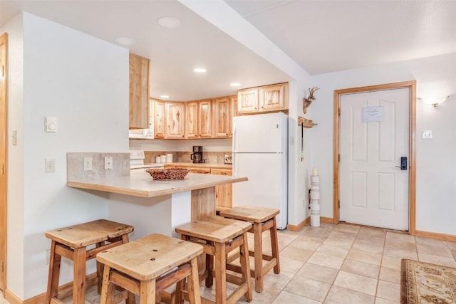 kitchen featuring kitchen peninsula, white appliances, light brown cabinets, light tile patterned floors, and a breakfast bar area