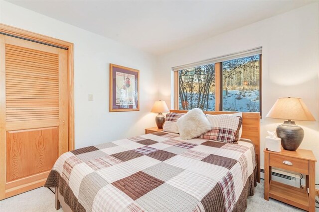 bedroom featuring a baseboard heating unit, light carpet, and a closet