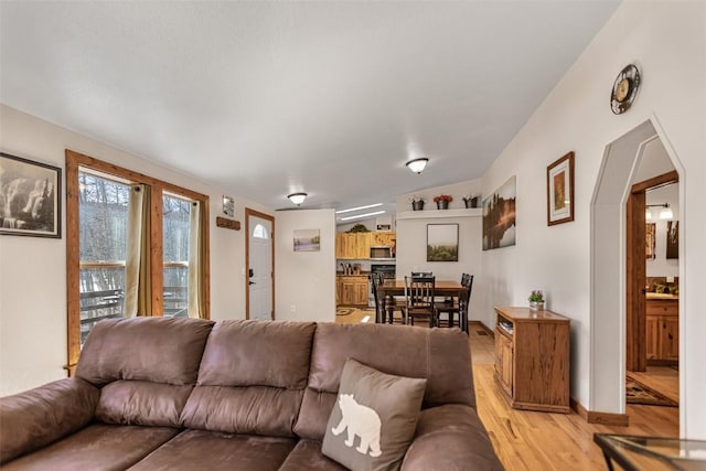 living room with arched walkways, baseboards, and light wood-style floors