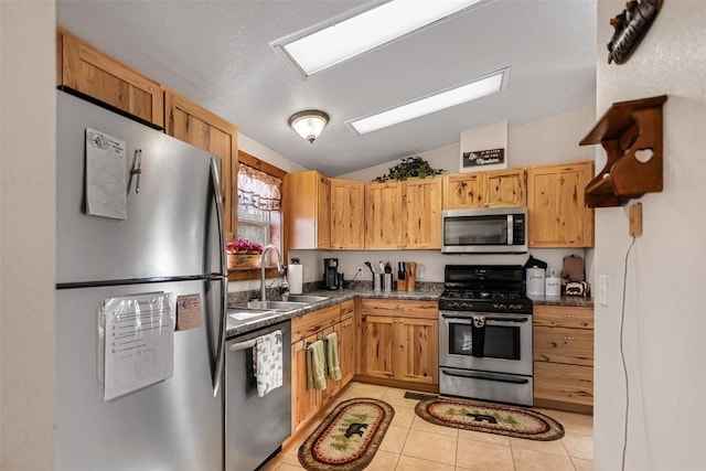 kitchen featuring light tile patterned floors, stainless steel appliances, dark countertops, vaulted ceiling, and a sink