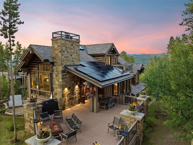 back house at dusk with solar panels and a wooden deck