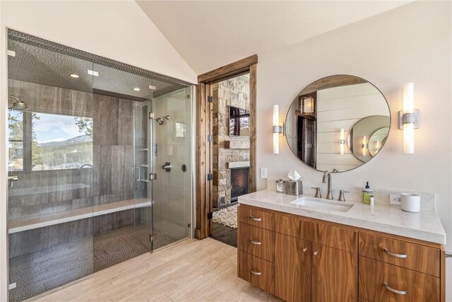 bathroom with hardwood / wood-style floors, vanity, vaulted ceiling, a fireplace, and an enclosed shower