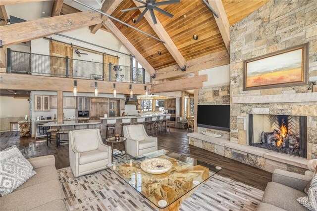 living room with beamed ceiling, wood-type flooring, high vaulted ceiling, and a stone fireplace