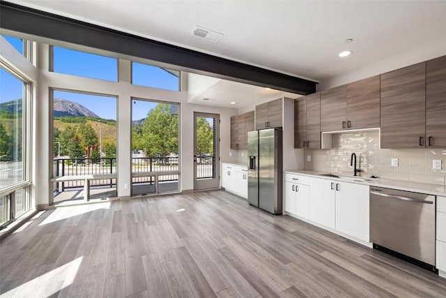 kitchen with appliances with stainless steel finishes, light wood-type flooring, tasteful backsplash, sink, and a mountain view