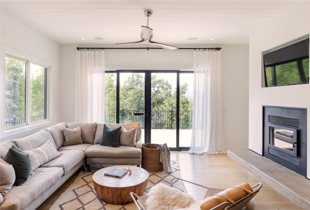 living room with recessed lighting, plenty of natural light, light wood-style floors, and a glass covered fireplace