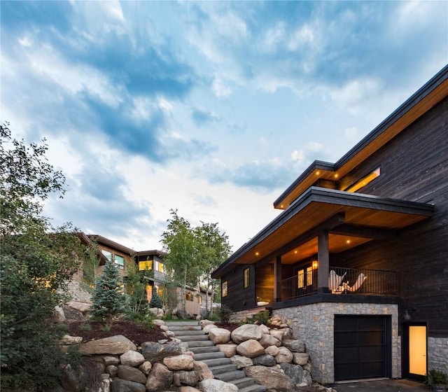 view of side of home featuring stairway, an attached garage, and stone siding