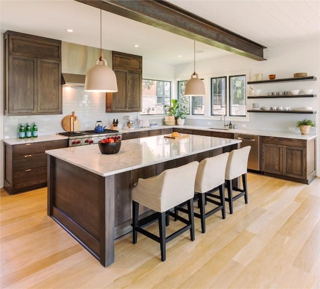 kitchen featuring beam ceiling, a kitchen breakfast bar, light hardwood / wood-style floors, a kitchen island, and appliances with stainless steel finishes