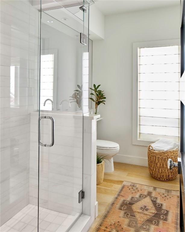 bathroom featuring a wealth of natural light, toilet, a shower with shower door, and hardwood / wood-style flooring