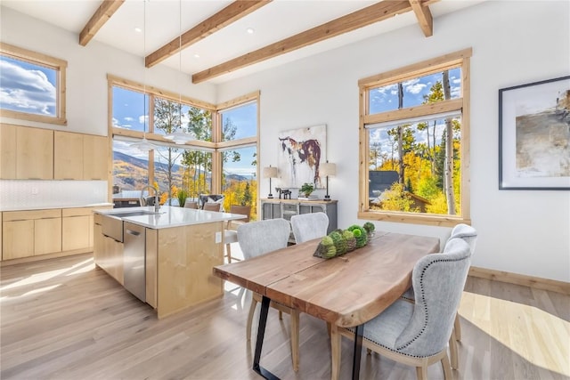 dining room featuring beamed ceiling, light wood-type flooring, a wealth of natural light, and sink