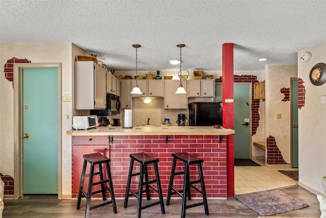 kitchen with black appliances, a breakfast bar area, hanging light fixtures, kitchen peninsula, and cream cabinets