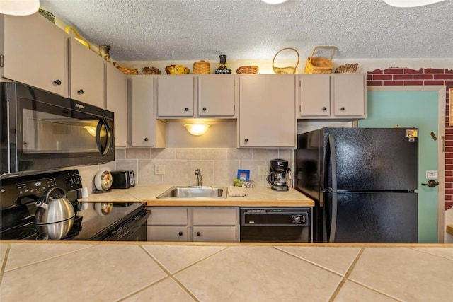 kitchen with tile countertops, tasteful backsplash, sink, black appliances, and a textured ceiling