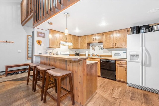 kitchen with pendant lighting, white appliances, a kitchen breakfast bar, sink, and light hardwood / wood-style flooring