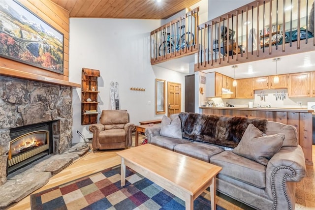 living room featuring wooden walls, high vaulted ceiling, wooden ceiling, a fireplace, and light hardwood / wood-style floors