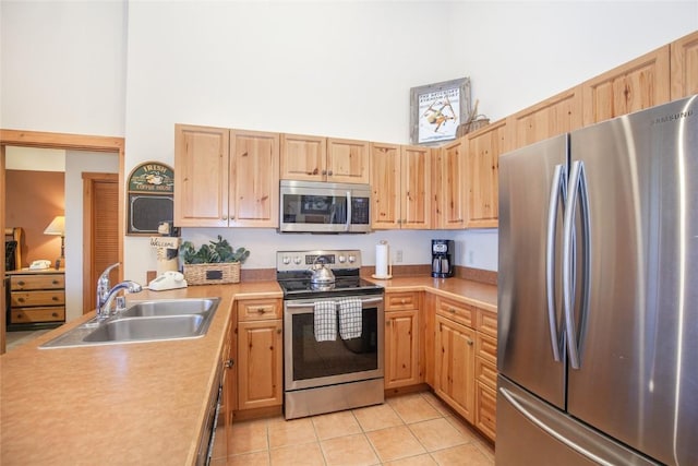 kitchen featuring a towering ceiling, light brown cabinetry, sink, light tile patterned floors, and stainless steel appliances