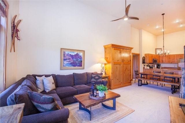 living room featuring a high ceiling, ceiling fan with notable chandelier, and light colored carpet