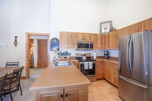 kitchen with sink, light tile patterned floors, appliances with stainless steel finishes, a high ceiling, and light brown cabinets