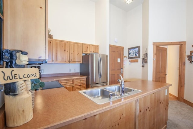 kitchen featuring a towering ceiling, sink, stainless steel fridge, light colored carpet, and light brown cabinets