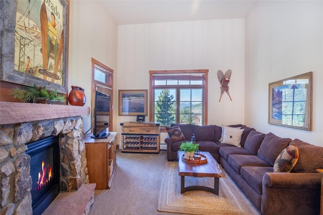 carpeted living room with a high ceiling and a stone fireplace