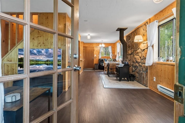 interior space with a wood stove, wood walls, dark hardwood / wood-style flooring, and a baseboard heating unit