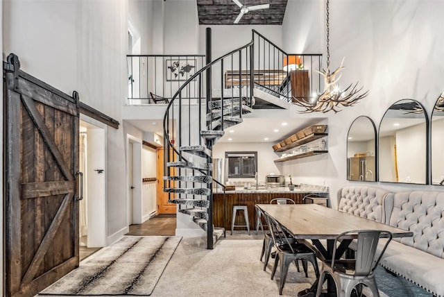 dining space featuring a towering ceiling, a barn door, and ceiling fan with notable chandelier