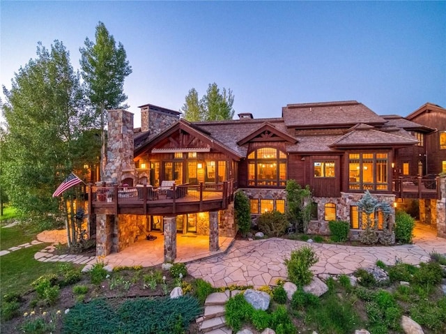 back house at dusk featuring a deck and a patio