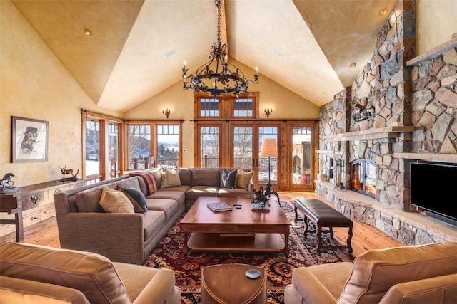 living room with a notable chandelier, a stone fireplace, hardwood / wood-style floors, and high vaulted ceiling