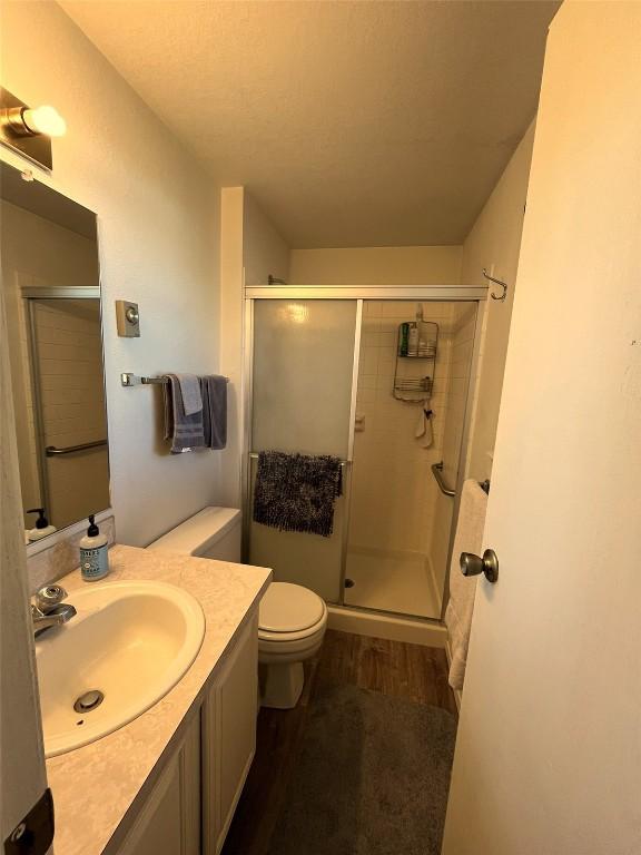 bathroom featuring vanity, toilet, wood finished floors, and a shower stall