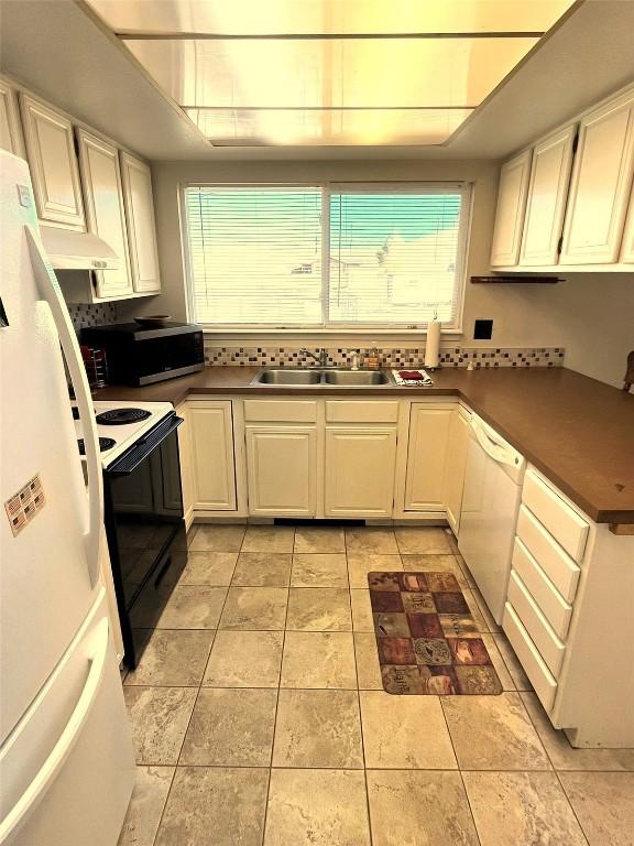 kitchen featuring dark countertops, light tile patterned floors, white cabinets, white appliances, and a sink