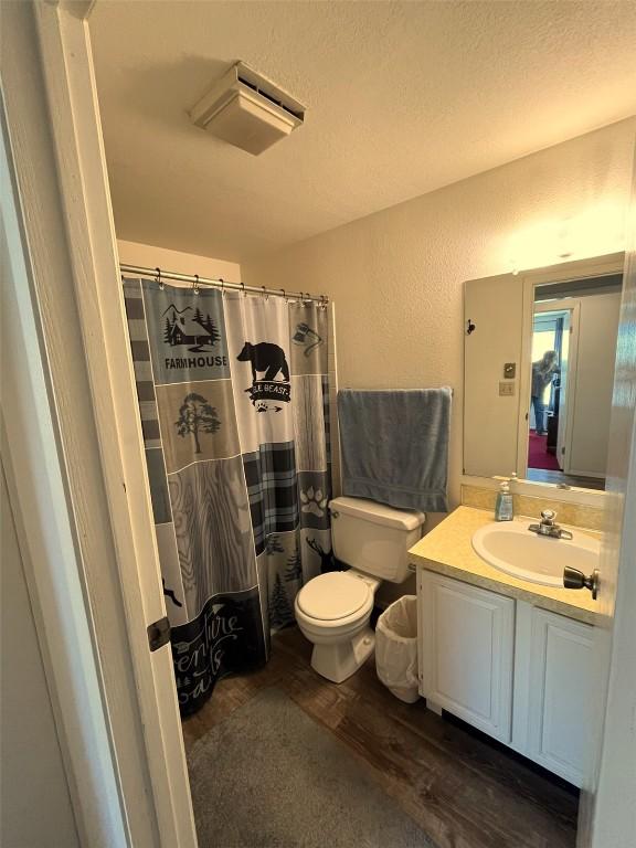 bathroom with toilet, vanity, wood finished floors, a textured wall, and a textured ceiling