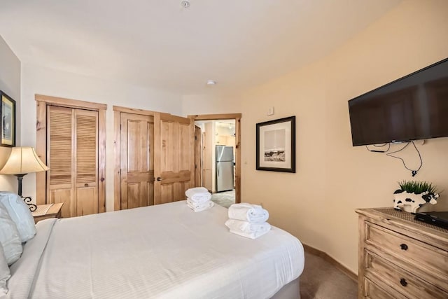 carpeted bedroom featuring stainless steel fridge and two closets