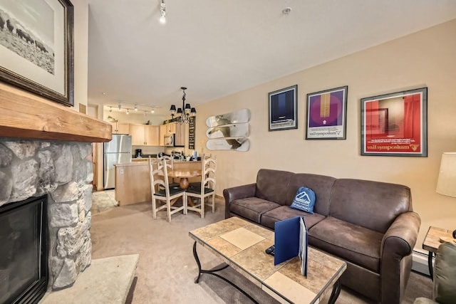 living room featuring rail lighting, light colored carpet, a baseboard heating unit, a notable chandelier, and a stone fireplace