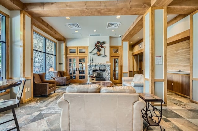 living room featuring beam ceiling, a stone fireplace, wooden walls, and french doors