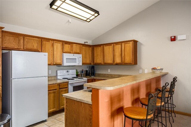 kitchen with white appliances, a breakfast bar area, a peninsula, vaulted ceiling, and brown cabinets