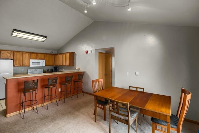 dining room with baseboards, lofted ceiling, and light carpet