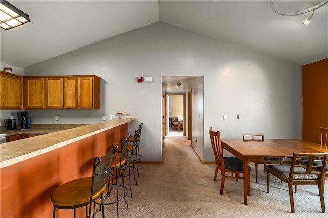 dining space with vaulted ceiling, light colored carpet, and baseboards