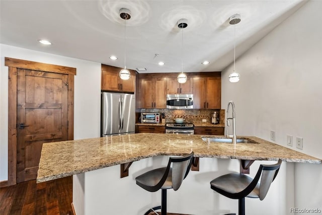 kitchen with sink, kitchen peninsula, decorative light fixtures, a breakfast bar, and appliances with stainless steel finishes