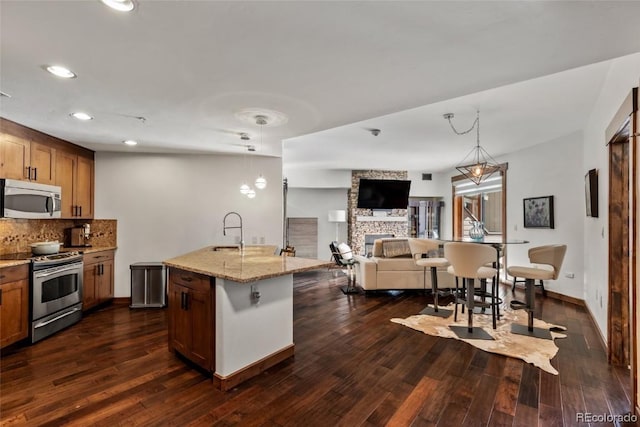 kitchen featuring dark wood-type flooring, hanging light fixtures, light stone countertops, a fireplace, and stainless steel appliances