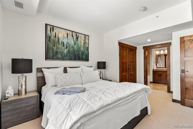 bedroom featuring ensuite bathroom and light carpet