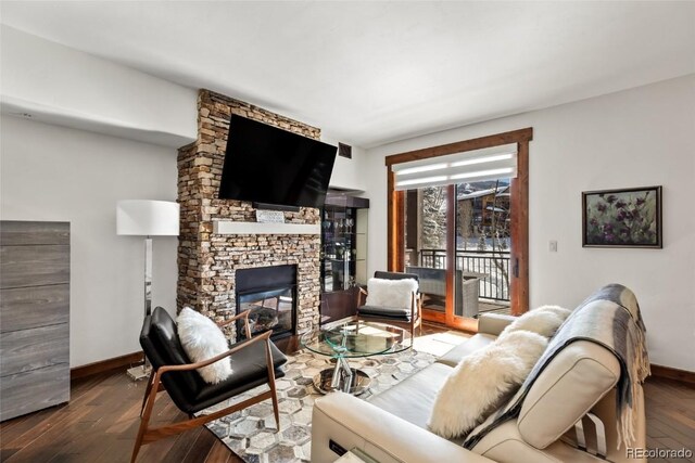 living room with a stone fireplace and dark wood-type flooring