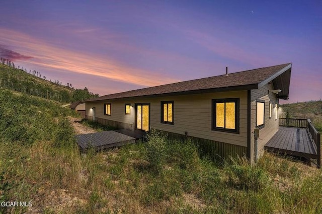 back house at dusk featuring a wooden deck