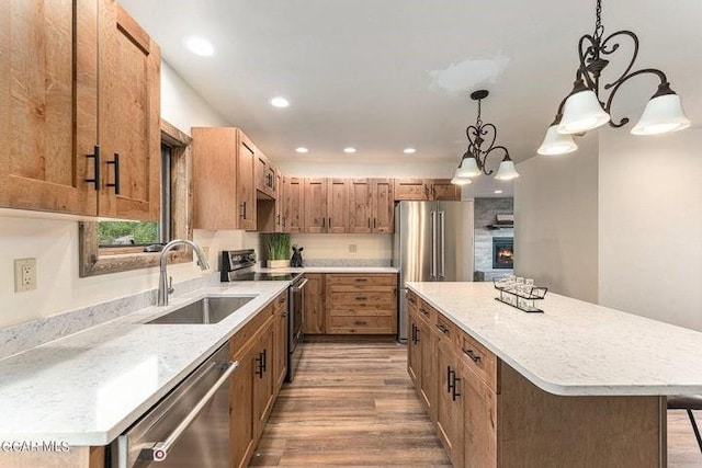 kitchen with appliances with stainless steel finishes, sink, pendant lighting, hardwood / wood-style floors, and a center island